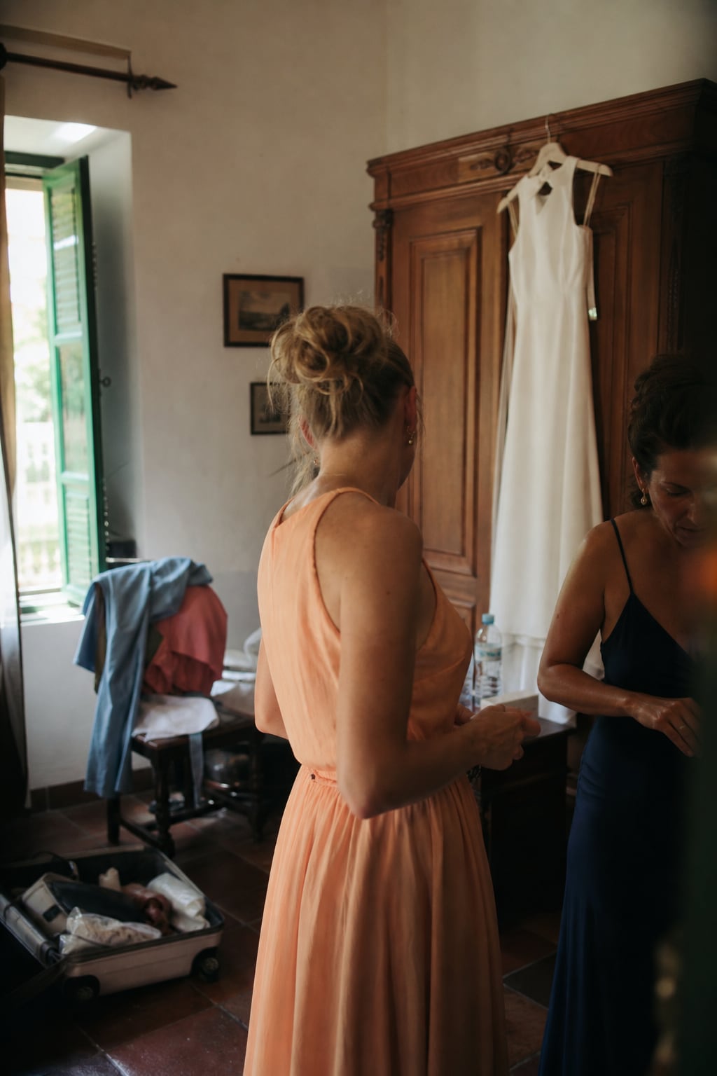 Bridesmaids getting ready beside the wedding dress hanging on an old wardrobe